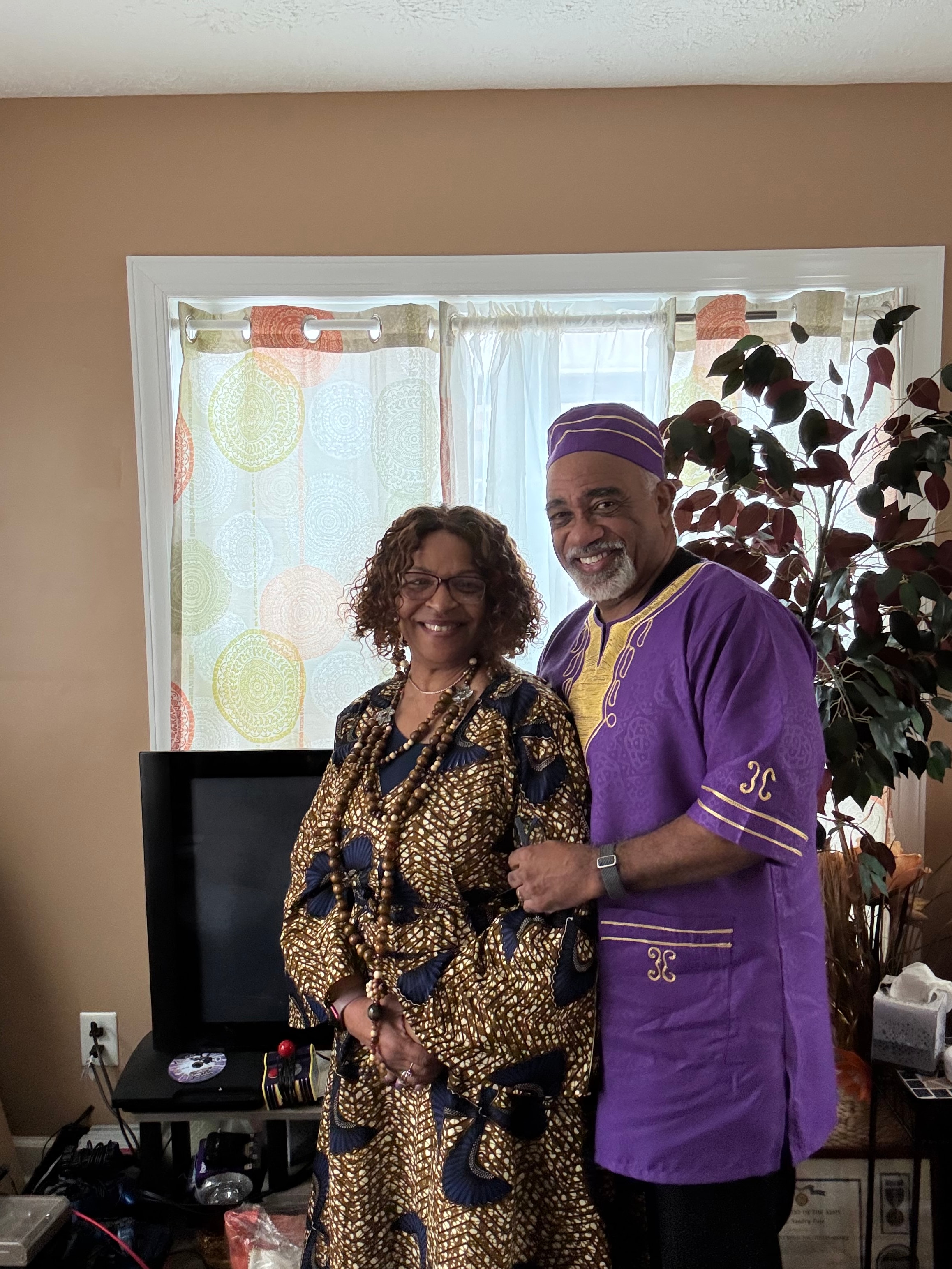 Pastor and First Lady in purple and gold traditional attire at home