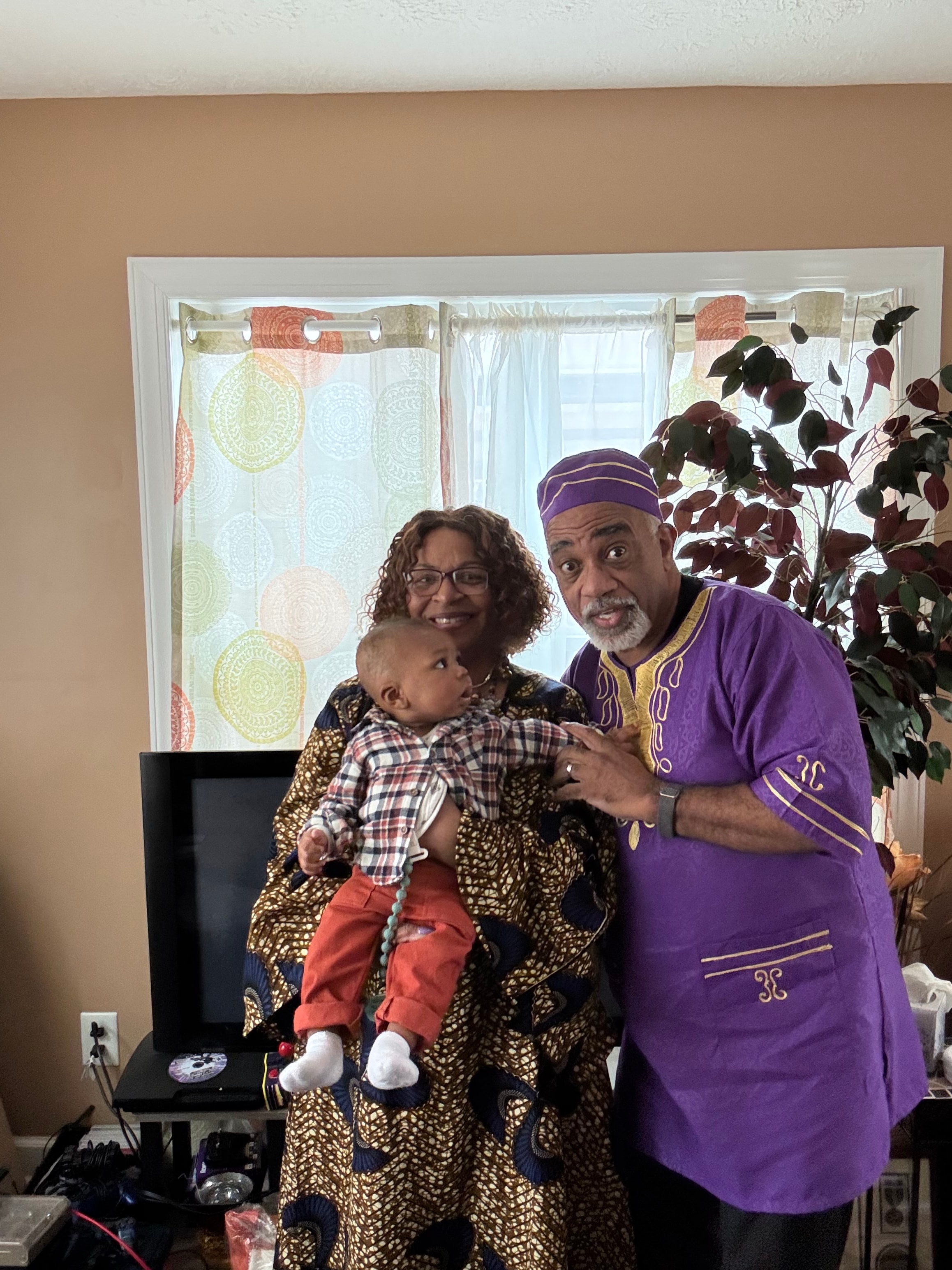 Pastor and First Lady with grandchild in purple and gold attire
